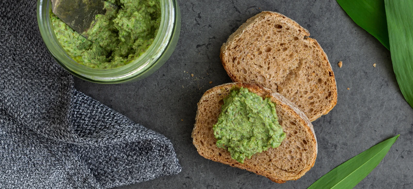Brot mit Bärlauch-Linsen-Aufstrich, daneben steht das Glas mit dem Aufstrich und einem Messer.