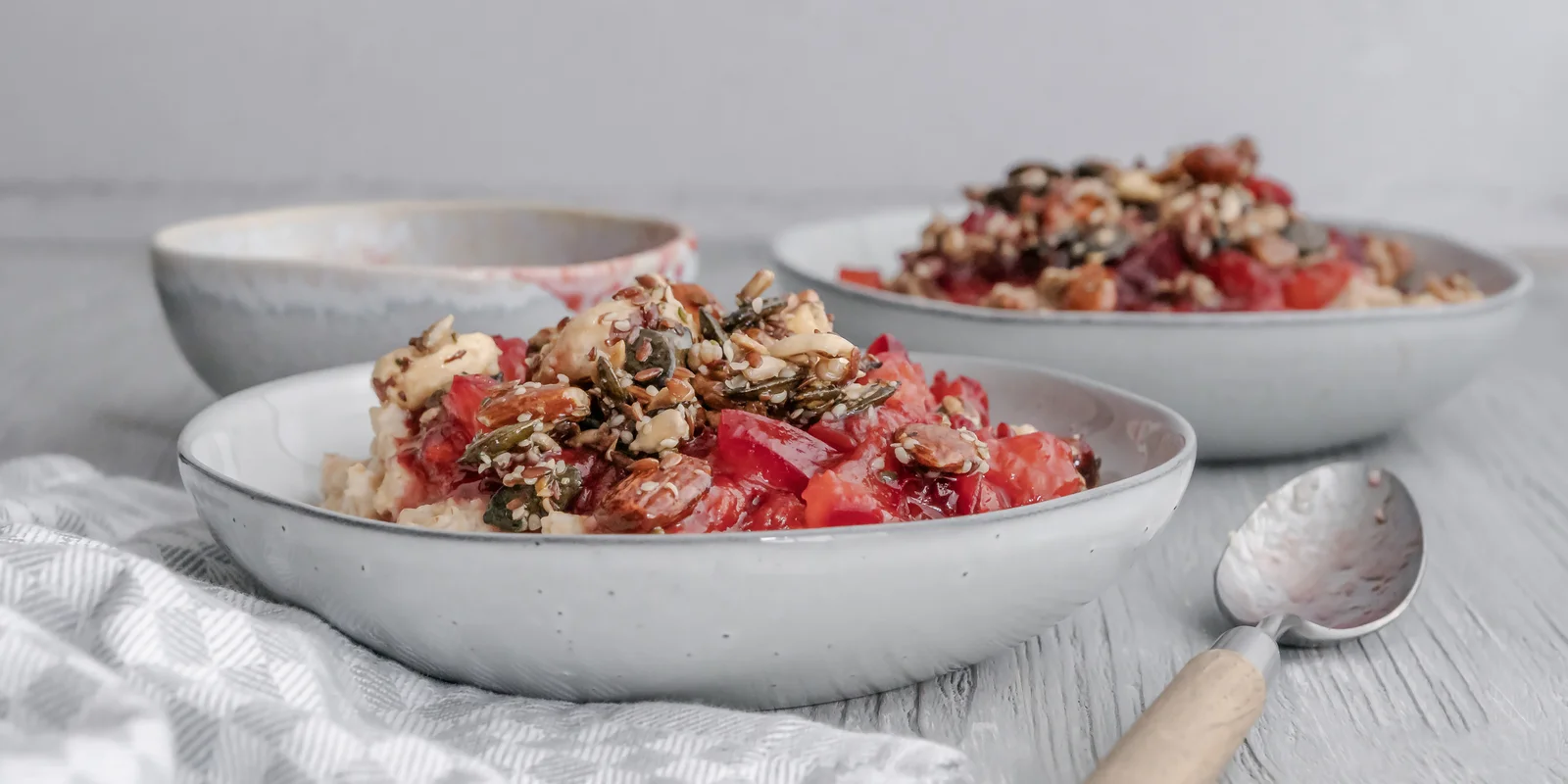 Warmes Frühstück aus Porridge, Pflaumenkompott und Nüssen mit einem Hauch Zimt.